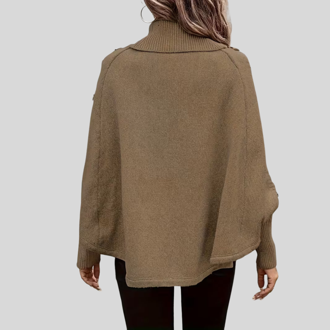 Rear view of the knitted poncho showing its broad shape, roll neck and curved lower edge.