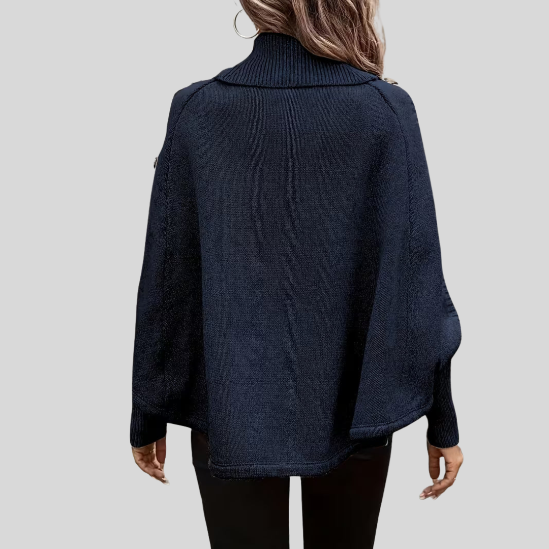 Rear view of the knitted poncho showing its broad shape, roll neck and curved lower edge.